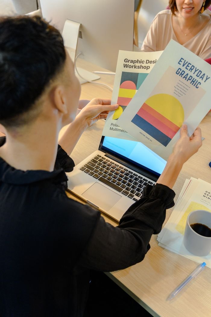 services-01 A professional reviews colorful graphic design brochures at a laptop in a modern office environment.