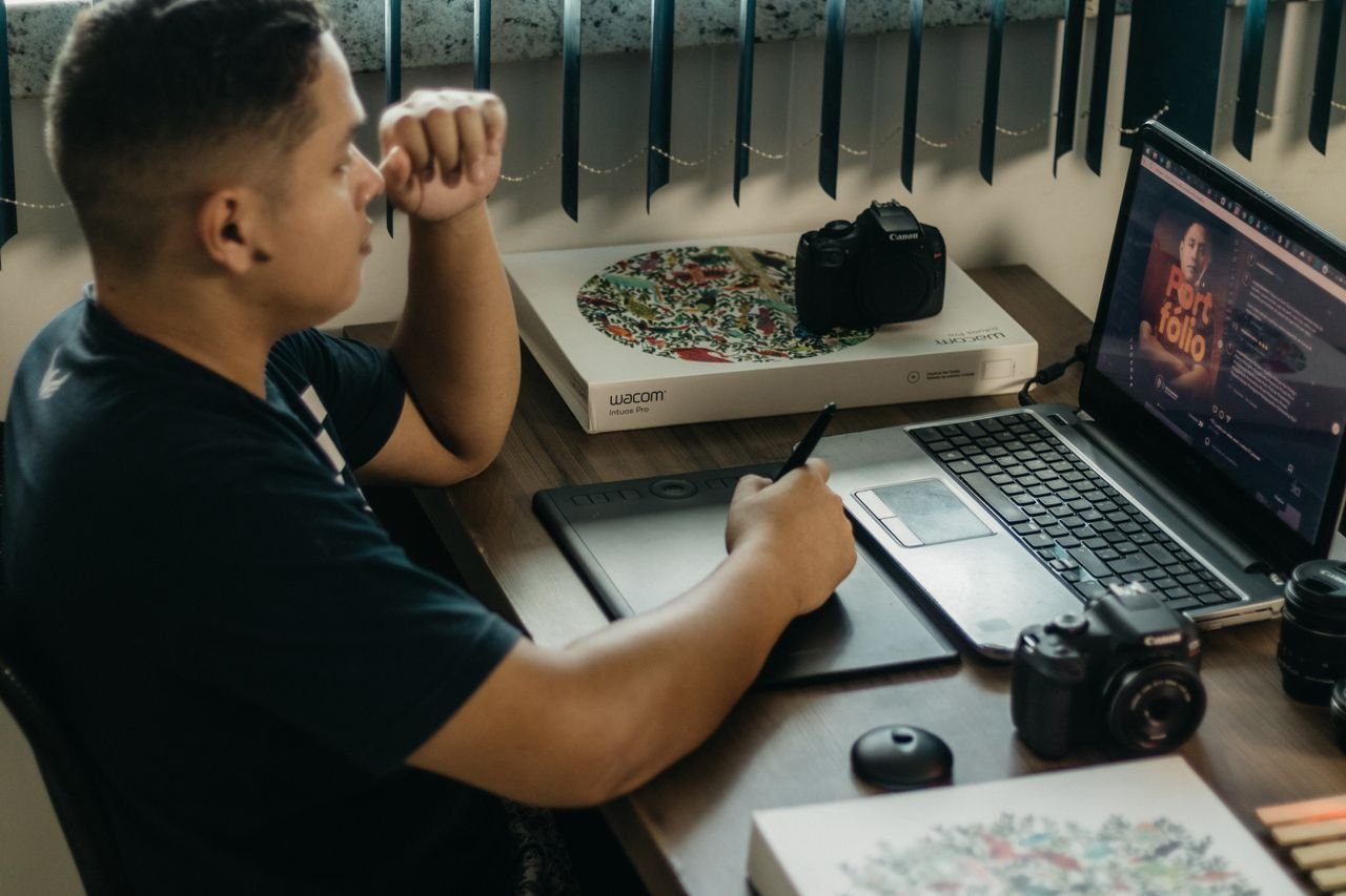 The Art of Drawing Readers In: Your attractive post title goes here A photographer working at a creative setup with a laptop and Wacom tablet, focused on editing photos indoors.
